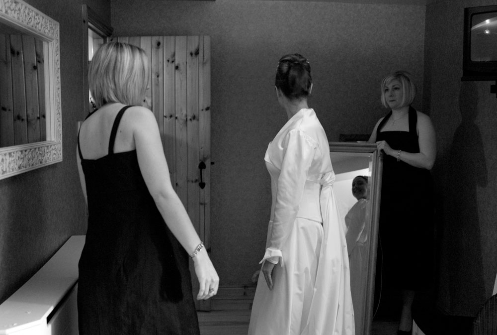 One bridesmaid holds the mirror for the bride to see her wedding dress