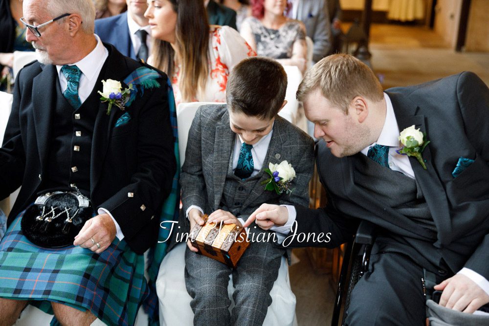Pageboy carrying wedding rings box with best man smiling at The Priests House.