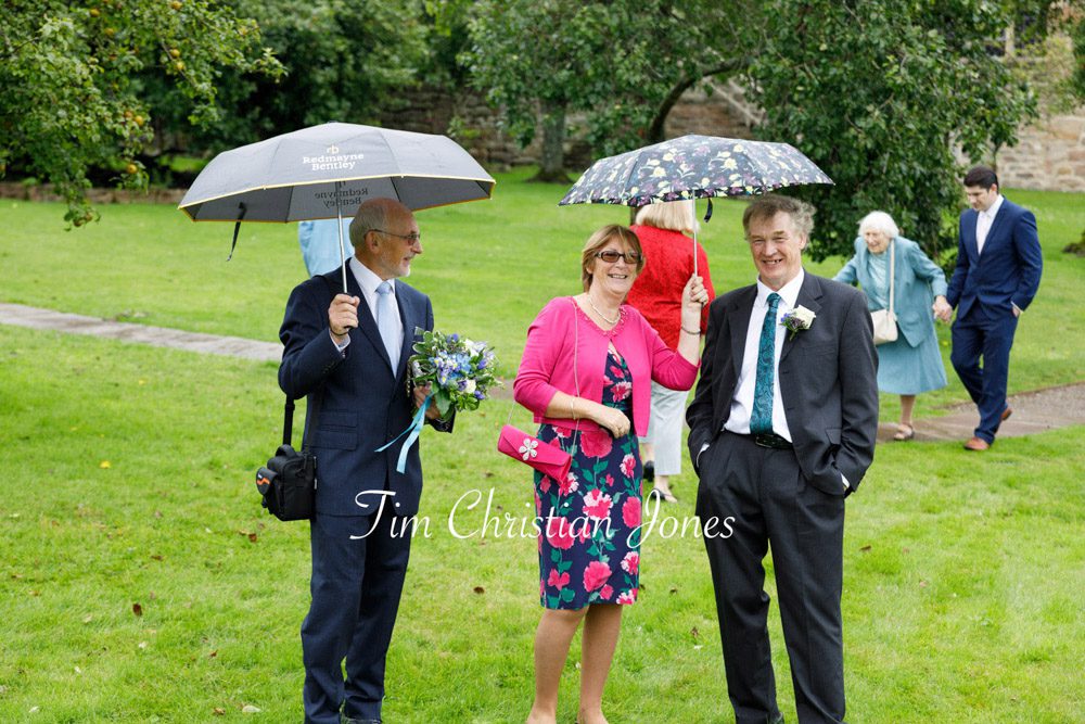Wedding guests gathered on the lawn with umbrellas at The Priests House, Barden Tower.