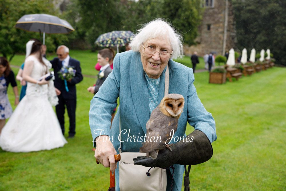 Candid wedding moment with bride's grandmother holding an owl at Barden Tower.