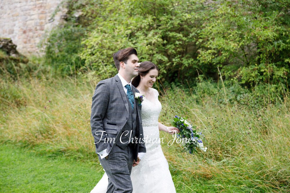 Natural wedding photo of couple walking through long grass.